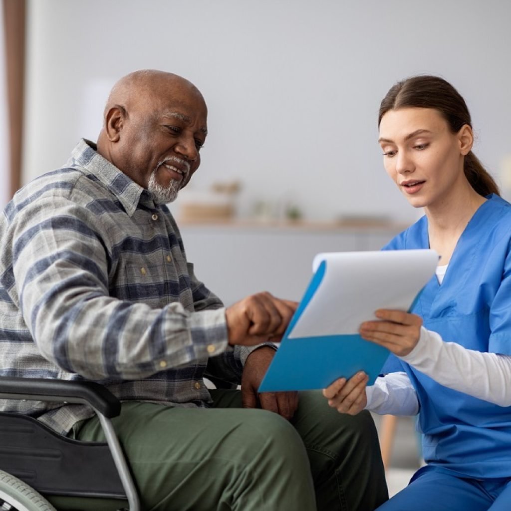 Attractive young woman in blue workwear nurse helping senior black man in wheelchair with questionnaire, african american pensioneer filling papers at nursing home, having assistance